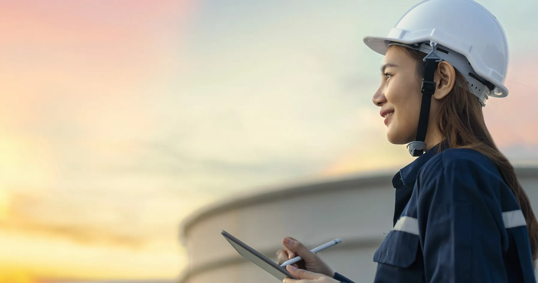 A woman wearing a hard hat, smiling and looking to the side.